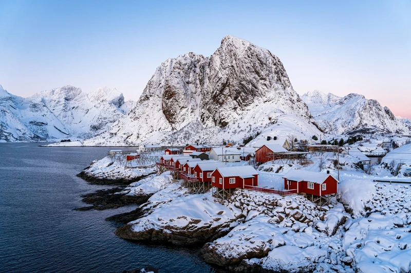 Rorbuer rossi in un villaggio innevato ai piedi di una montagna, nelle Lofoten.