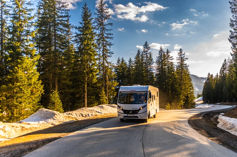 Camper su una strada nel bosco tra pini e chiazze di neve.