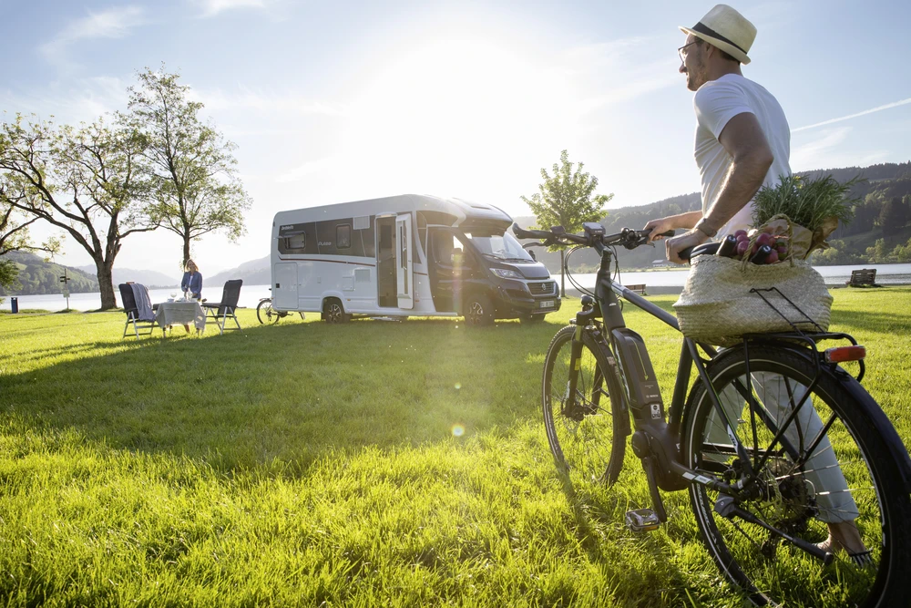 Ciclista descansando en una bici eléctrica en un prado, con una autocaravana aparcada detrás