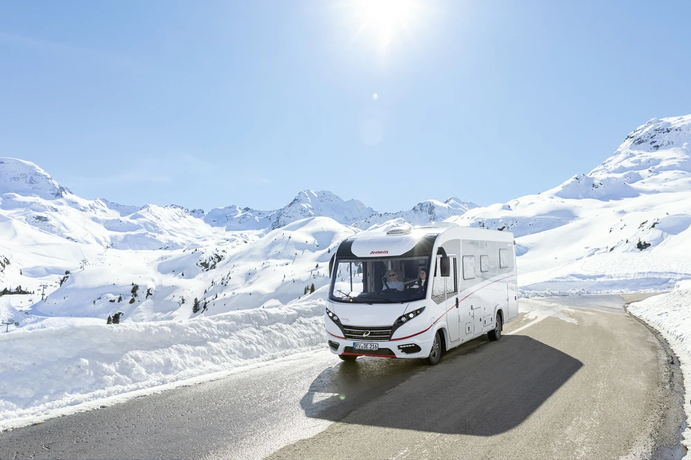 Autocaravana en una carretera de montaña entre cumbres nevadas en un día soleado