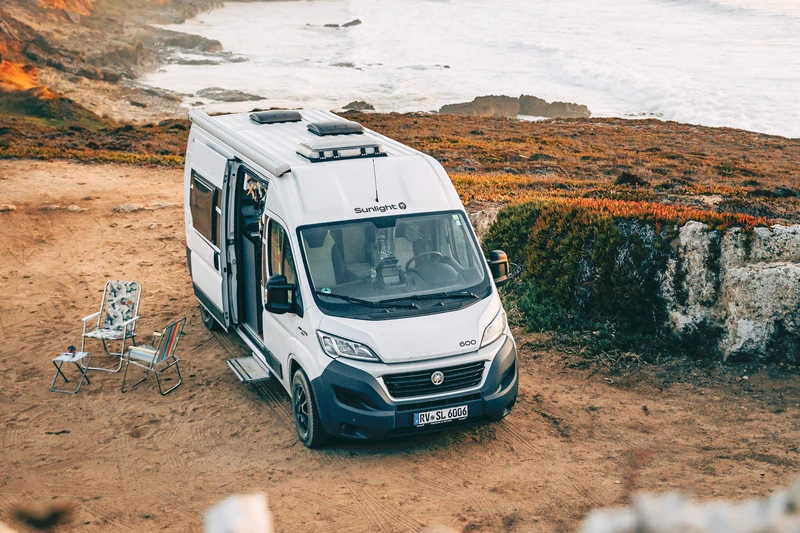 Van aménagé garé sur une côte rocheuse, avec des chaises de camping à côté