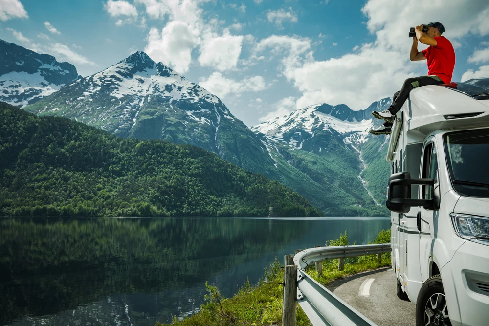 Voyageur avec des jumelles sur le toit d’un van aménagé, au-dessus d’un fjord