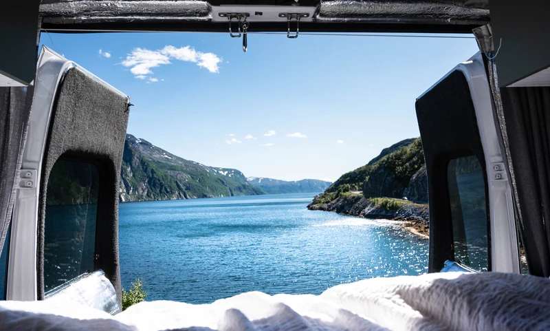 Vue sur un fjord depuis le lit d’un van aménagé, portes arrière ouvertes