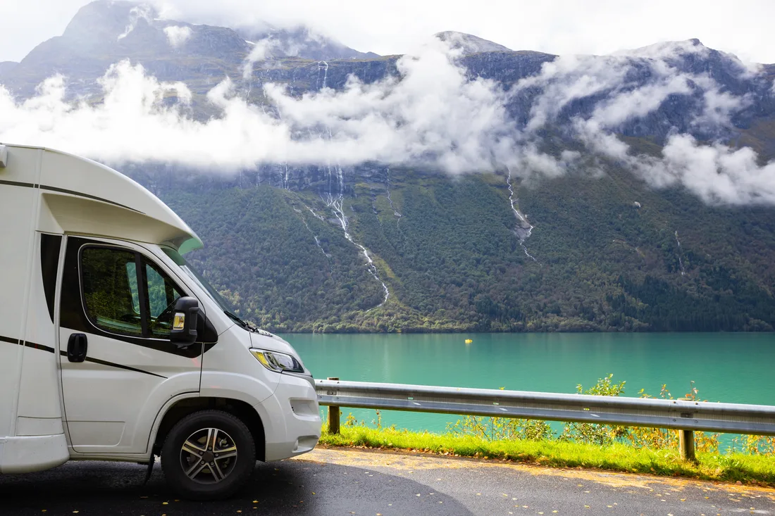 Camping-car garé au bord d’un fjord turquoise, sous des montagnes dans les nuages