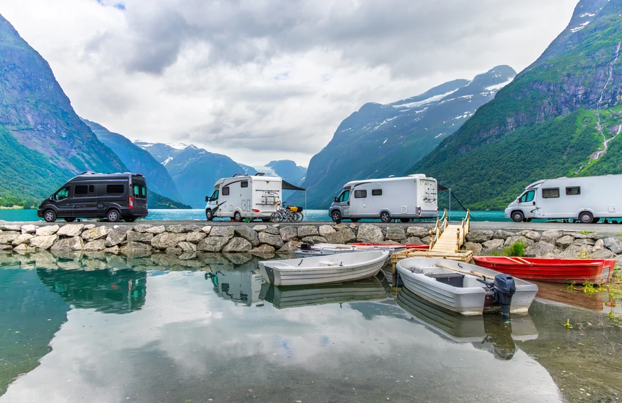 Camping-cars garés au bord d’un fjord, avec des barques amarrées devant