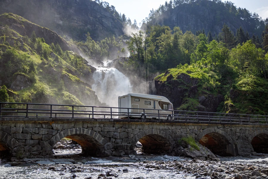 Camping-car traversant un pont de pierre devant une cascade
