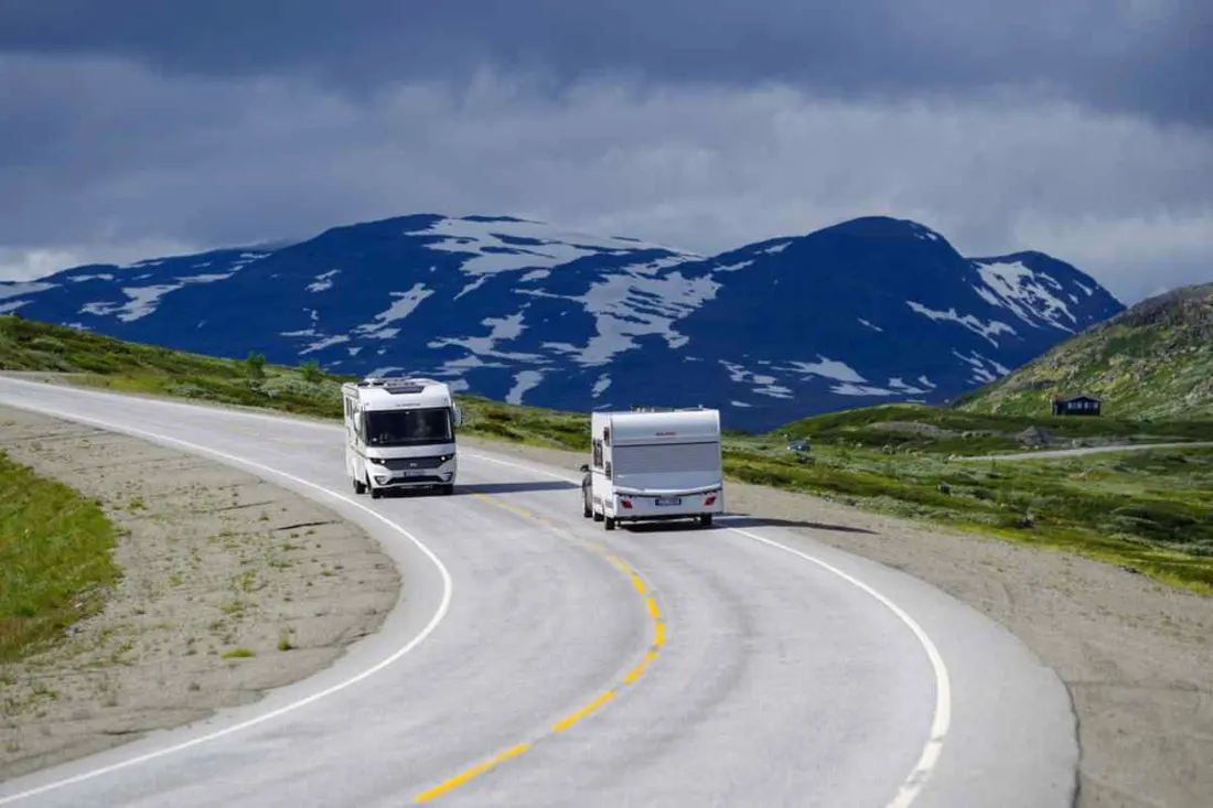 Two motorhomes on a mountain road with snow-patched peaks behind