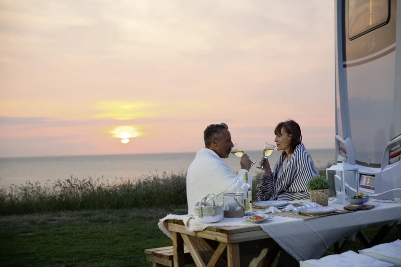 Couple dînant à une table de camping à côté de son camping-car au coucher du soleil