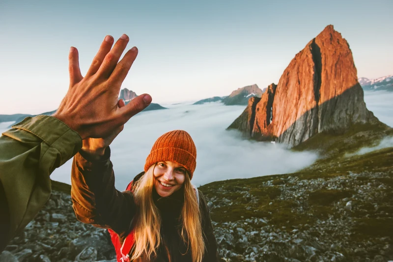 Voyageuse souriante qui tape dans la main au sommet d'une montagne, au-dessus des nuages