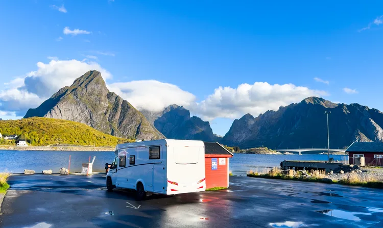 Camping-car garé à côté d’une cabane rouge au bord de la mer, au pied de montagnes escarpées