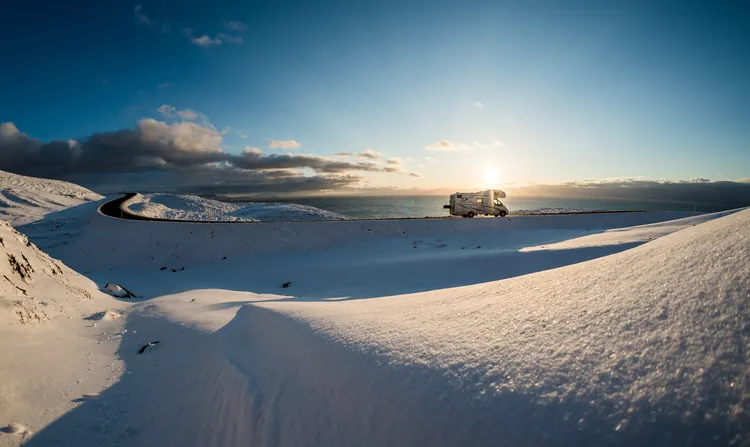 Camping-car sur une route enneigée, le soleil bas sur l’horizon