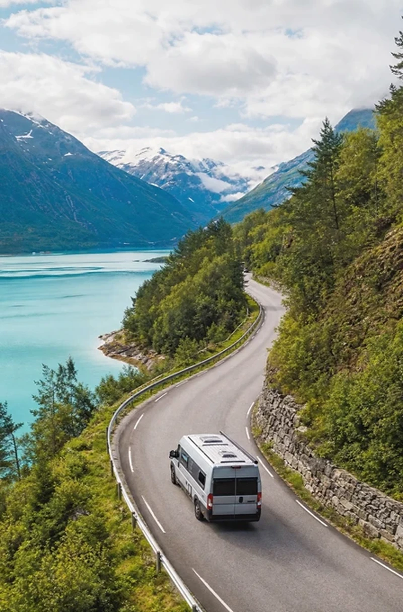 Camping-car sur une route sinueuse au-dessus d'un fjord turquoise en Norvège