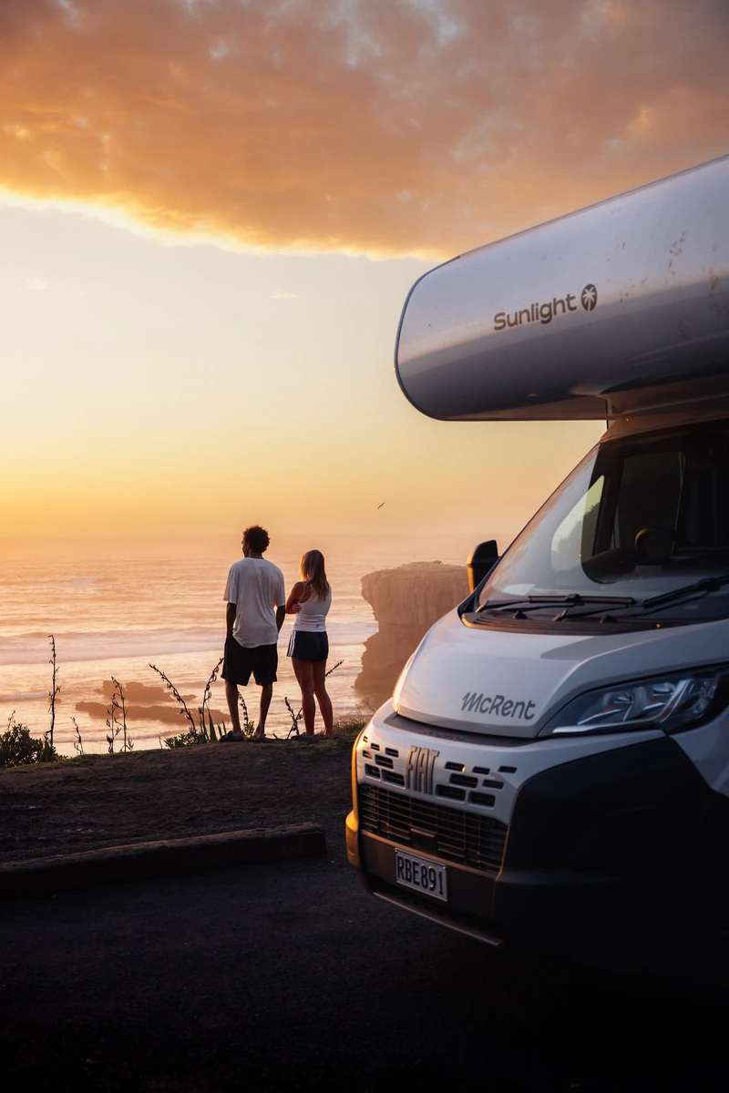 Couple regardant le coucher de soleil sur la mer à côté de son camping-car