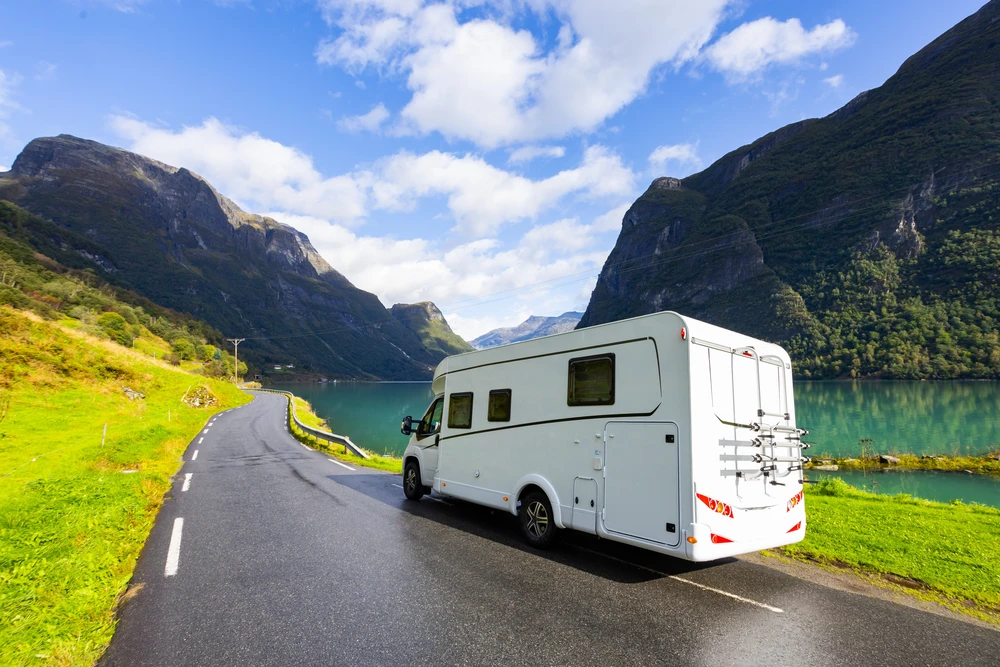 Camping-car sur une route au bord d’un fjord, entre des montagnes verdoyantes