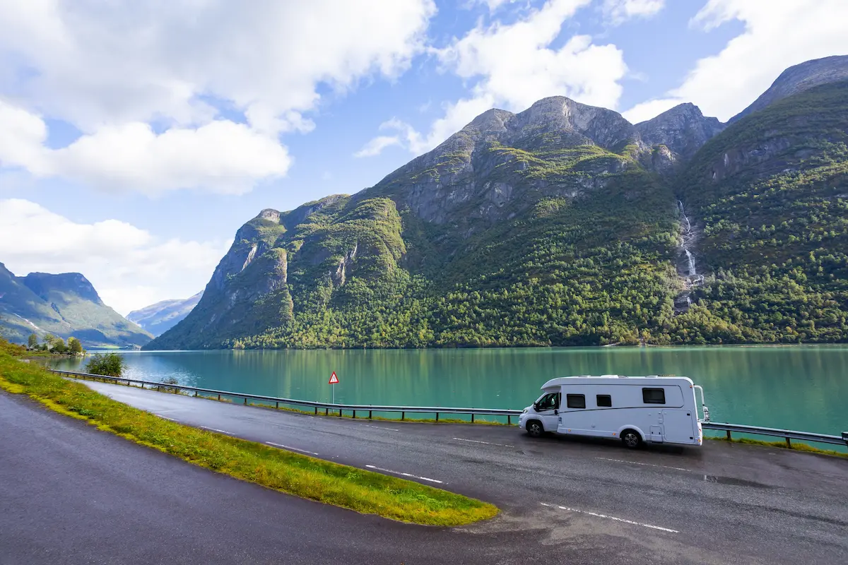 Autocaravana en una carretera junto a un fiordo turquesa bajo montañas verdes