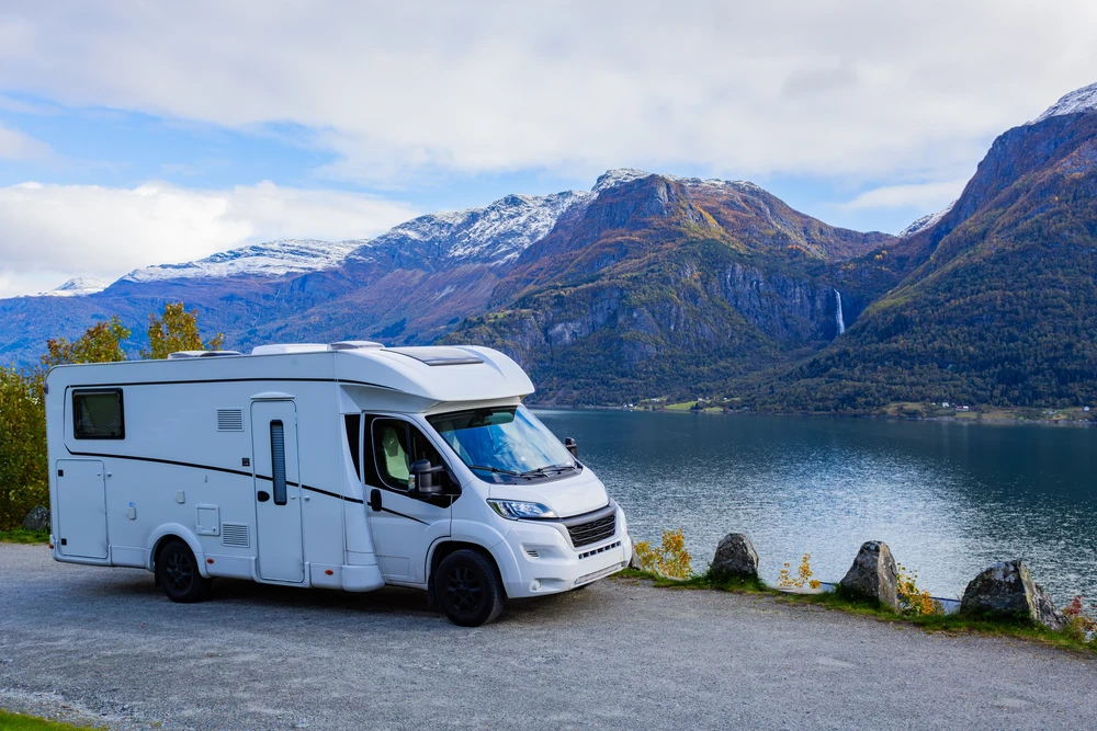Autocaravana aparcada junto a un fiordo bajo montañas nevadas